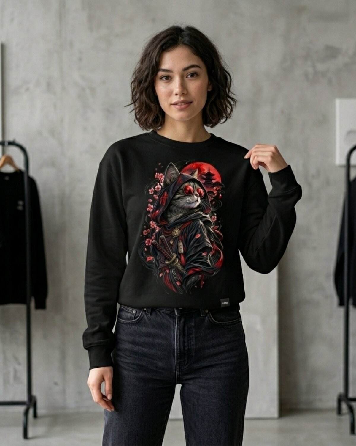 Woman wearing black gothic samurai cat crewneck sweatshirt with red moon and cherry blossoms, standing in a concrete studio